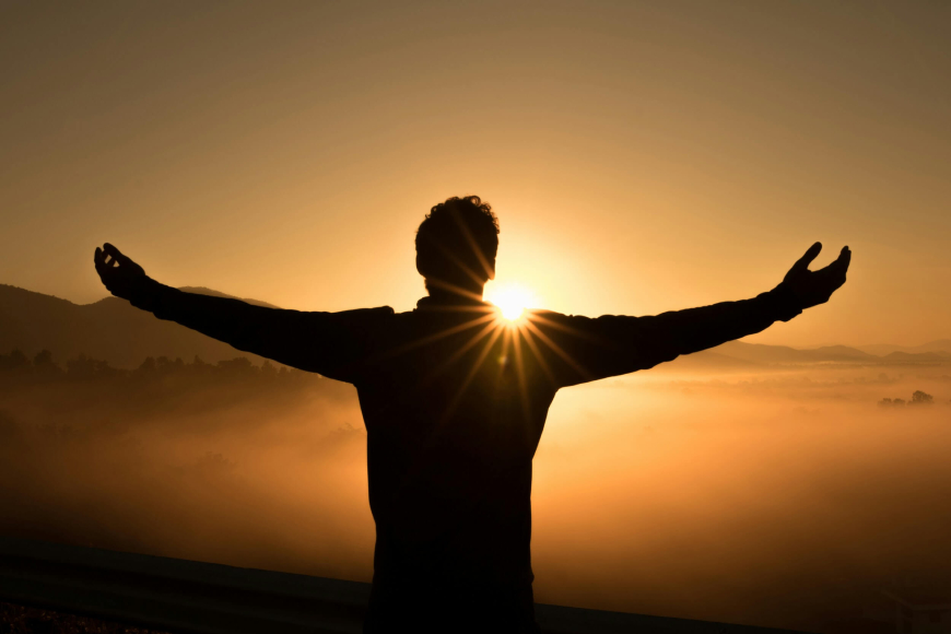 A man stands with arms outstretched, silhouetted against a bright sun, symbolizing freedom and connection with nature.